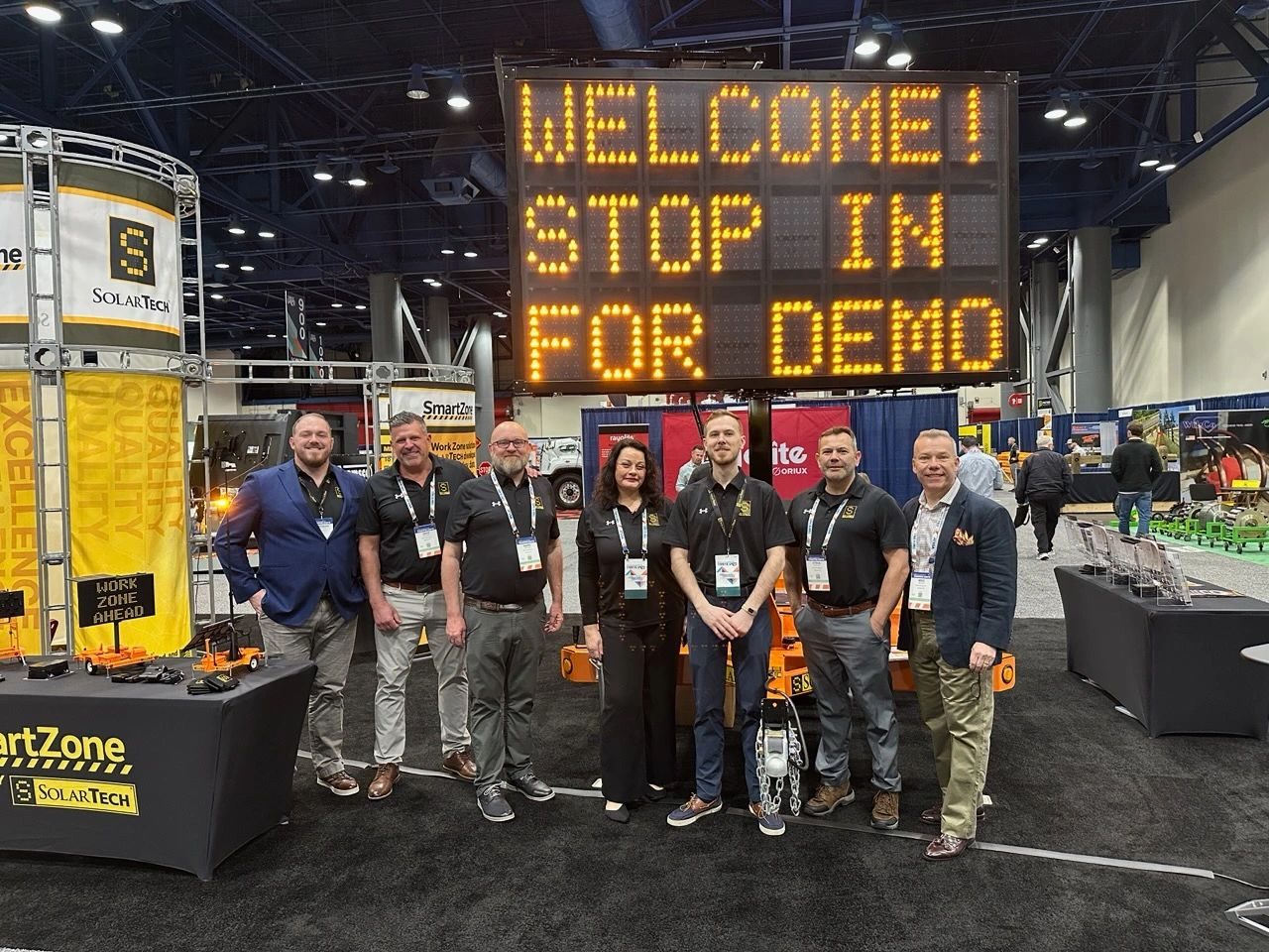 The SolarTech team at a trade show booth, standing in front of a message board that reads Welcome! Stop in for demo